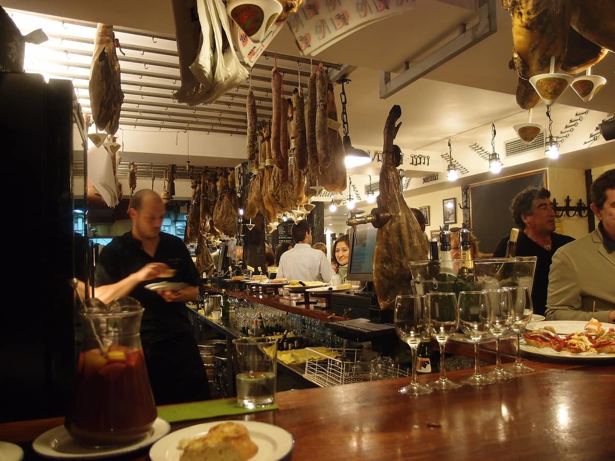 A pintxos bar counter in San Sebastián, with hams hanging above the bar
